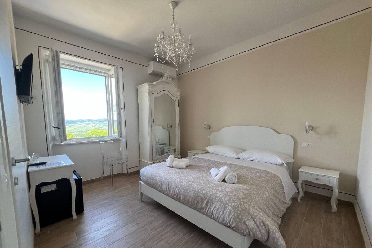 A bedroom with a bed, a desk, a chair, a dresser, and a chandelier.