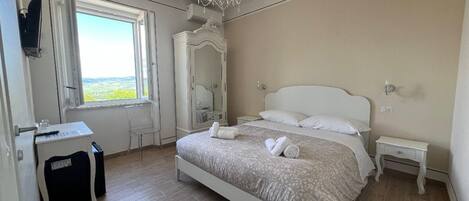 A bedroom with a bed, a desk, a chair, a dresser, and a chandelier.