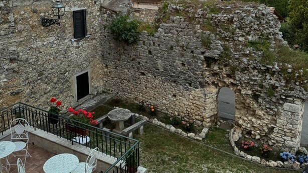 A stone building with a balcony, a small table, and chairs. - Dimora dei Magi (Saturnia)