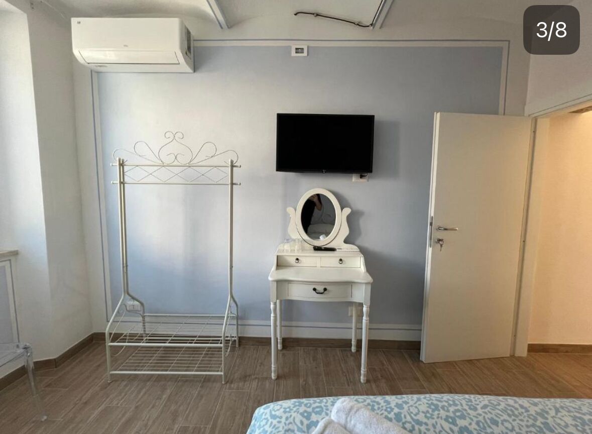 A bedroom with a bed, a vanity with a mirror, a TV on the wall, and a door.