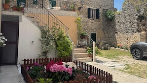 A stone building with a staircase leading to a balcony, surrounded by a garden with a wooden fence. - Dimora dei Magi (Saturnia)