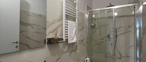 Un baño moderno con salpicadero de mármol, un espejo grande, un lavabo blanco, dos inodoros y una ducha con mampara de vidrio.