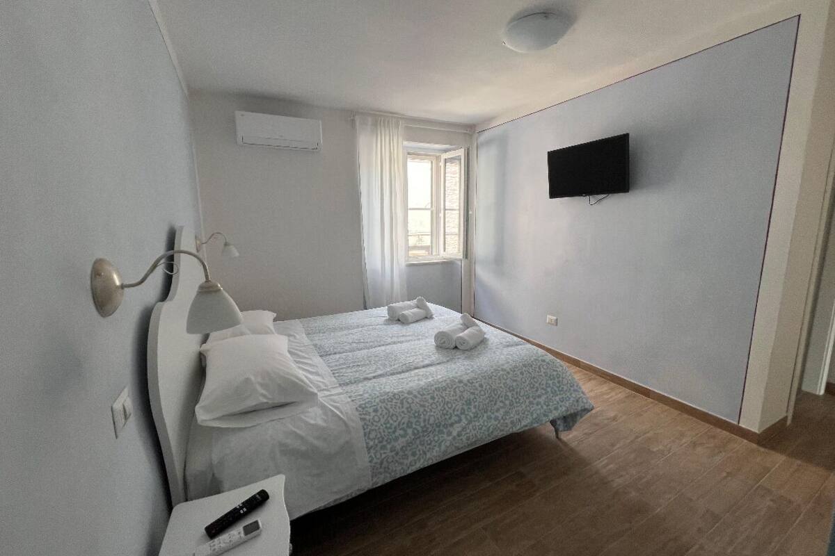 A hotel room with a bed, a desk, a lamp, a TV, and a window.