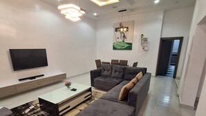 A modern living room with a sectional sofa, a flat-screen TV, a coffee table, and a dining area.