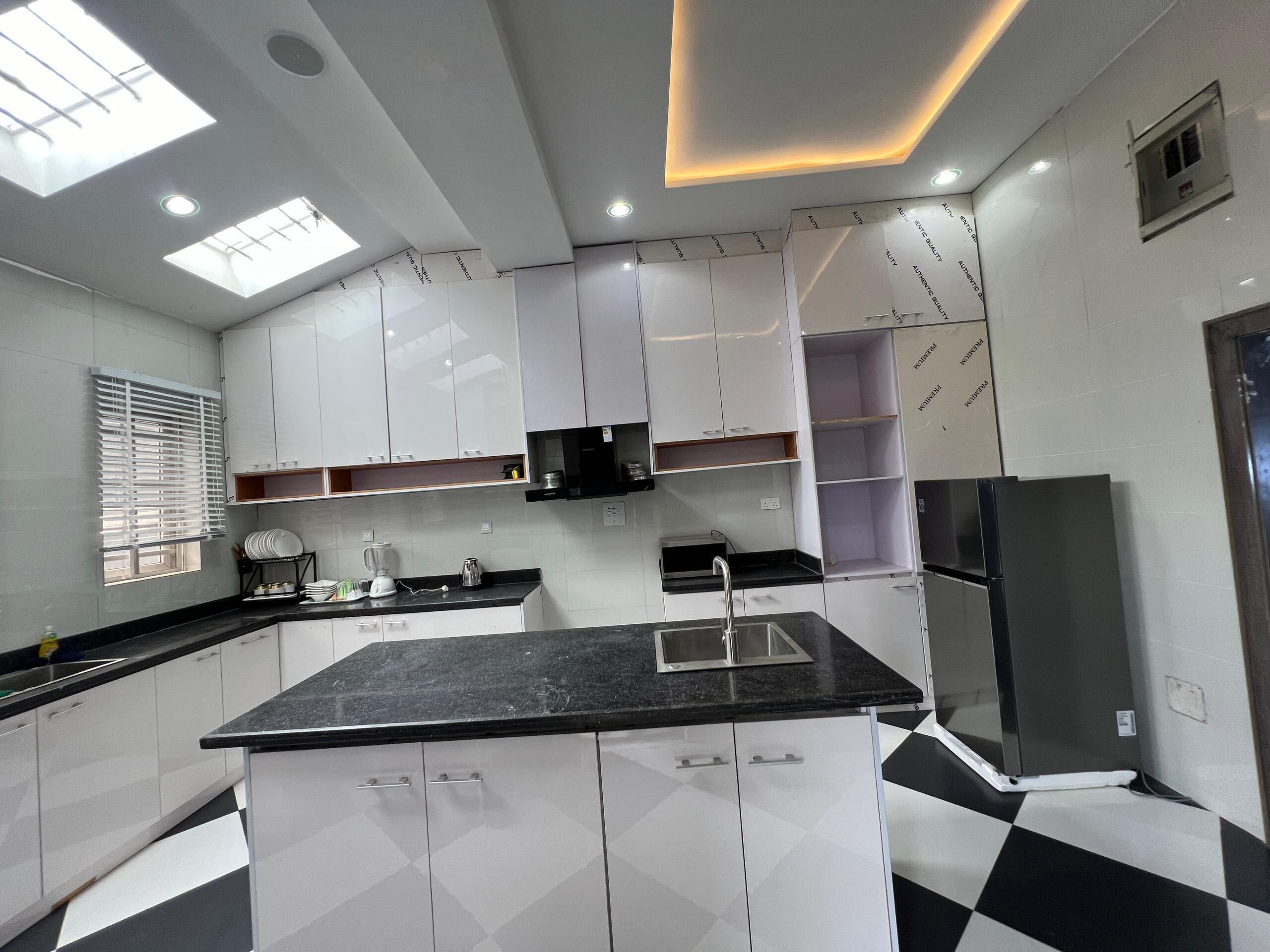 A modern kitchen with white cabinets, a black countertop, and a black and white checkered floor.