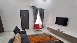 A modern living room with a black sofa, a red chair, a large rug, a TV, and an air conditioning unit.