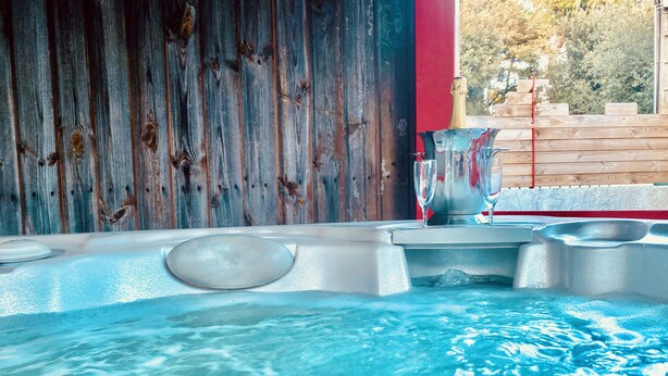 Un bain à remous avec un mur en bois en arrière-plan, une bouteille et des verres.