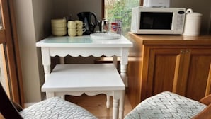 Een kleine keuken met een witte tafel en een bankje, een magnetron en een koffiezetapparaat.