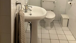 Een kleine, schone badkamer met een wit wastafel, toilet en een raam boven het toilet.