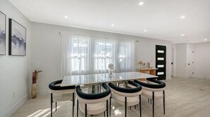 Ein moderner Essbereich mit einem Glastisch, weißen Stühlen und einer Blumenvase.