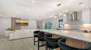 Eine moderne Küche mit einer großen Kochinsel, Barhocker und einem Essbereich mit einer Couch.
