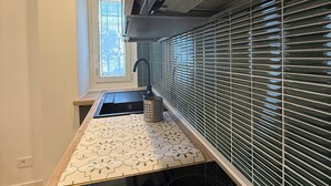 Een moderne keuken met een zwart fornuis, een raam met zonwering en een roestvrijstalen afzuigkap.