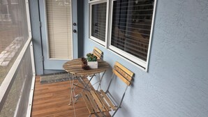 Ett träbord med stolar och en krukväxt på en veranda med en blå vägg och ett fönster med persienner.