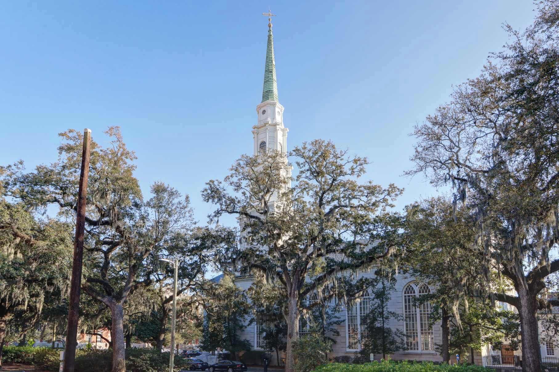 Eine Kirche mit hohem Kirchturm und einem Uhrturm, umgeben von Bäumen.