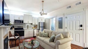 A compact living space with a kitchenette, a sofa, a glass coffee table, and a patterned rug. - 1872 Historic King Suite | Live Oak Views! (Savannah)