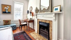 A room with a fireplace, a desk, a chair, and a bed. - 1872 Historic King Suite | Live Oak Views! (Savannah)