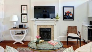 A living room with a fireplace, a television, and a dining area. - 1872 Historic King Suite | Live Oak Views! (Savannah)