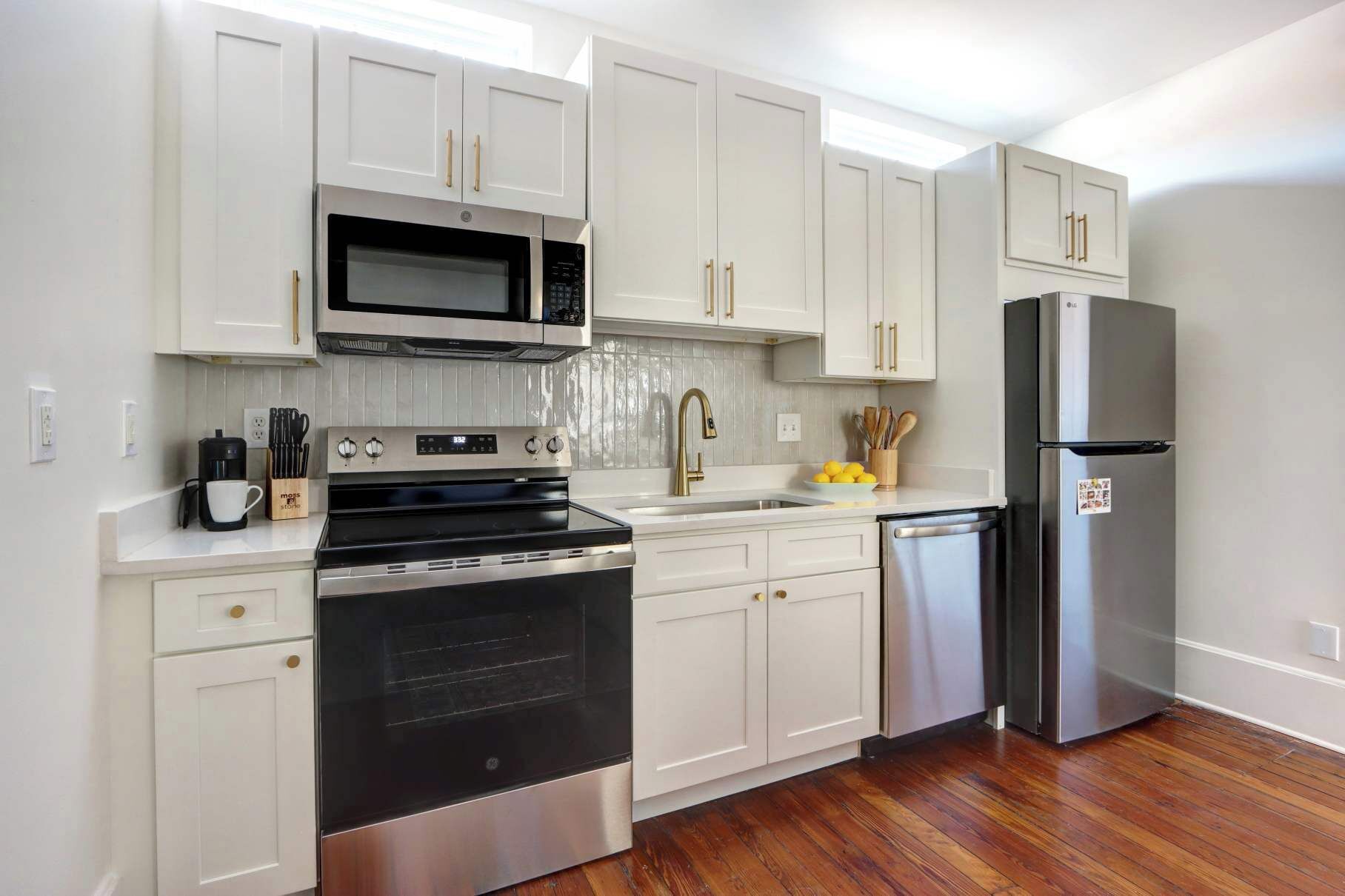 A modern kitchen with white cabinets, stainless steel appliances, and wooden flooring.
