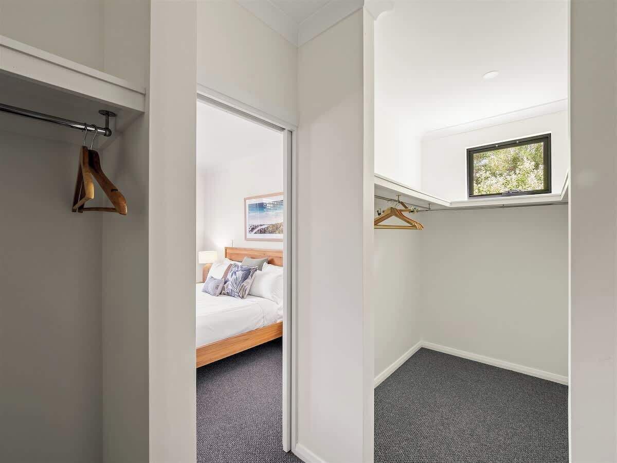 A bedroom with a bed, a closet with wooden hangers, and a small window.