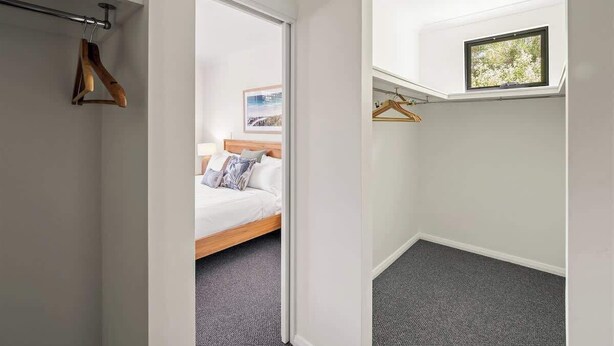 Une chambre à coucher avec un lit, une armoire avec des cintres en bois et une petite fenêtre.