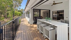 Une terrasse extérieure avec un espace barbecue, un coin salon extérieur blanc avec des bancs rembourrés et un ventilateur de plafond.