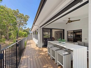 Eine Terrasse im Freien mit Barbereich, einer weißen Sitzgruppe im Freien mit gepolsterten Bänken und einem Deckenventilator.