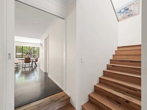 A modern interior with a wooden staircase, a dining area with chairs and a table, and a large window. - Trailside Vista—Modern Comfort near Geographe Bay (Dunsborough)