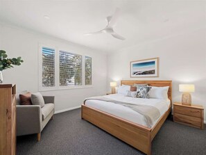 Ein Schlafzimmer mit einem hölzernen Bett, zwei Nachttischen, einem Deckenventilator, einem Fenster mit Jalousien und einem gerahmten Bild an der Wand.