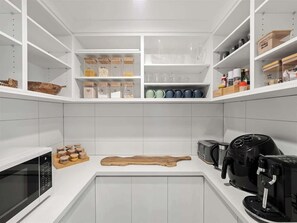 Una cocina moderna con armarios blancos, microondas, cafetera y tabla de cortar.