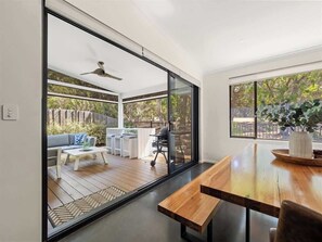 A modern interior with a wooden dining table, a sofa, and a glass sliding door leading to an outdoor patio. - Trailside Vista—Modern Comfort near Geographe Bay (Dunsborough)