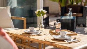 A wooden table with plates, cups, and a coffee pot, set in a bright, sunlit room with wicker furniture and a vase of flowers. - Villa Selvatic with Sea Views, Pool, Sauna, and Cinema (Arenas)