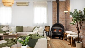 A cozy living room with a sofa, a small table, a potted plant, a fireplace, and a brick wall. - Villa Selvatic with Sea Views, Pool, Sauna, and Cinema (Arenas)