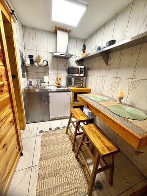 A compact kitchen with a microwave, toaster oven, and sink. There is a wooden bench and a small table with a placemat. - Rustic Studio 7! Pets Welcome! (Pigeon Forge)