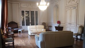 Een ruime woonkamer met een kroonluchter, houten vloeren en klassiek meubilair, waaronder een bank en fauteuils.