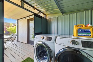 A laundry area with two front-loading washing machines, a yellow detergent container, and a patio with a table and chairs. - Private yard|AC|EV| Relocation| Remote work (San Diego)