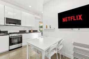 A modern kitchen with white cabinetry, a built-in oven, and a dining area with a white table and chairs. - Private yard|AC|EV| Relocation| Remote work (San Diego)