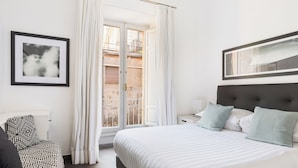 Une chambre avec un grand lit, une table de chevet, une chaise et une fenêtre avec des rideaux.