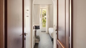 Un couloir étroit mène à une chambre qui contient un lit, une commode et une fenêtre avec des rideaux.