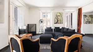Un salon moderne avec un canapé d’angle, deux fauteuils en bois, une lampe sur pied et des œuvres d’art accrochées aux murs.