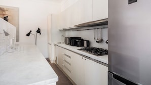 Une cuisine moderne avec des meubles blancs, un réfrigérateur en acier inoxydable, une cuisinière à gaz et une machine à café.