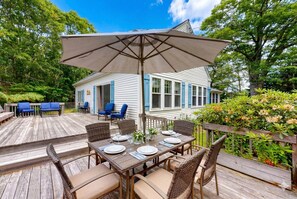 A wooden deck with a dining table set for six, surrounded by wicker chairs. - Harbor View House | Walk to Water (Boothbay Harbor)