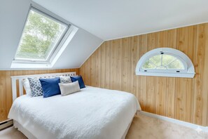 A bedroom with a sloped ceiling, a skylight, and a dormer window.