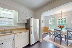 A modern kitchen with white cabinetry, a stainless steel refrigerator, and a dining area with a table and chairs.