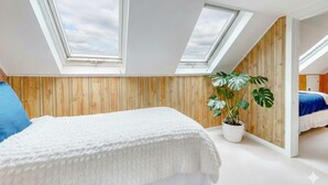 Una camera da letto con un lucernario, pareti rivestite in legno, un letto con coperta bianca, cuscino blu e una pianta in vaso.