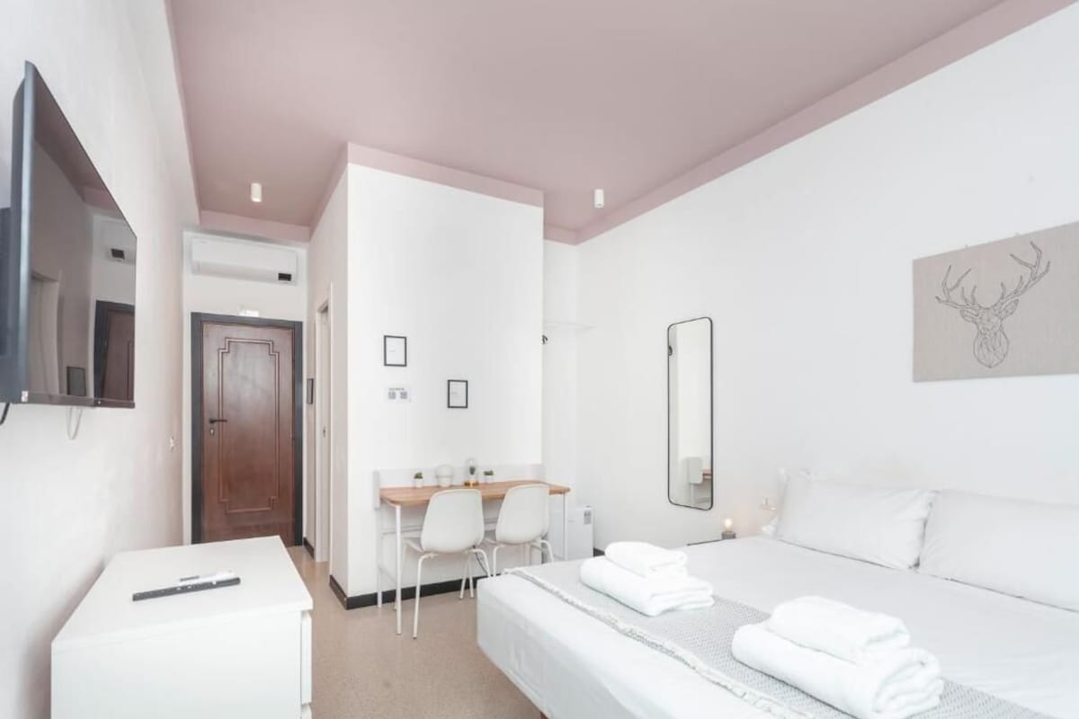 Hotellihuone, jossa on sänky, työpöytä, tuoli, televisio ja peili.