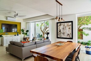 A modern living room with a sofa, dining table, and chairs, a TV, and a ceiling fan. - New! Cap Cana Apartment w/ Exclusive Pool & Terrace (Punta Cana)