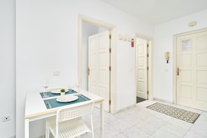 Un petit coin repas avec une table dressée pour deux personnes, une chaise blanche et une porte dont la clé est dans la serrure.