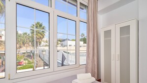 Ein Schlafzimmer mit großem Fenster, einem Bett mit weißer Decke und einem Kleiderschrank.