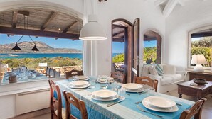 Un coin repas avec une table dressée pour quatre personnes, un canapé et une vue sur la mer.