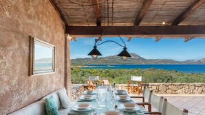 Une table dressée pour le dîner, avec vue sur la mer et les collines.